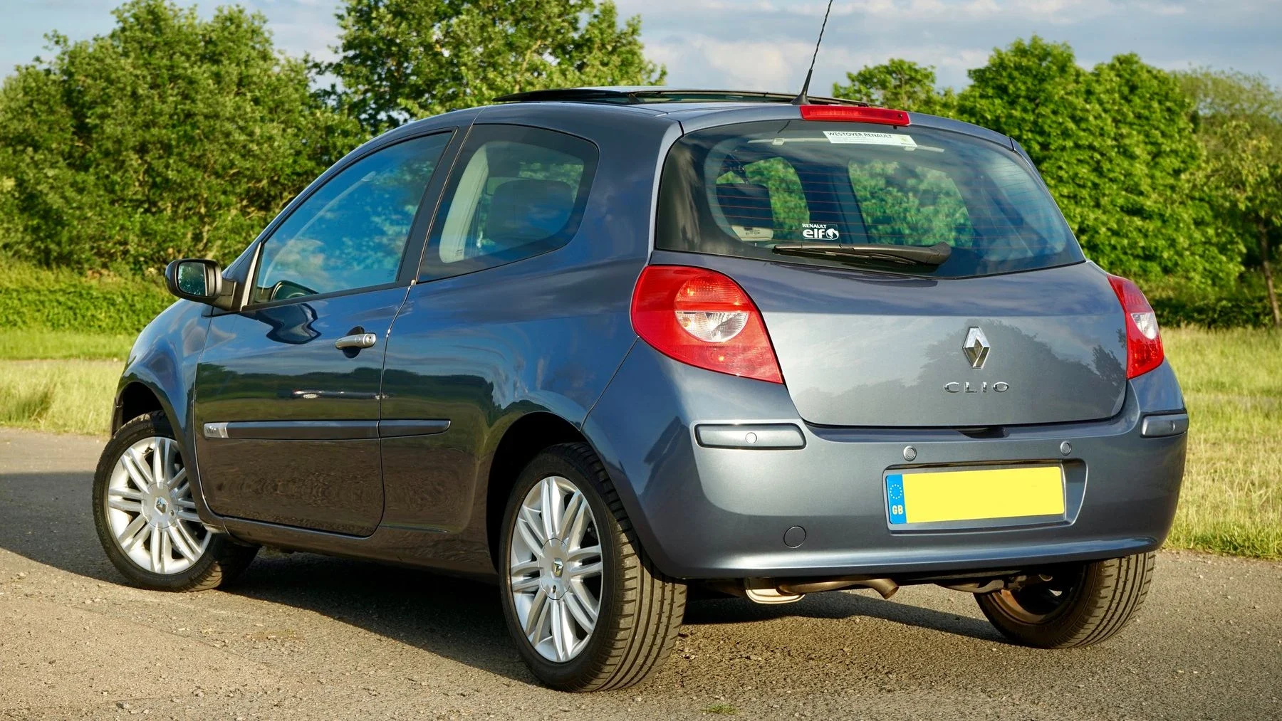Grey hatchback seen from the rear beside trees