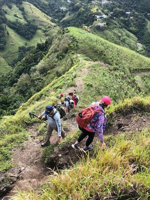 Caminantes en fila por un sendero en una ladera de hierba de la Cordillera Central