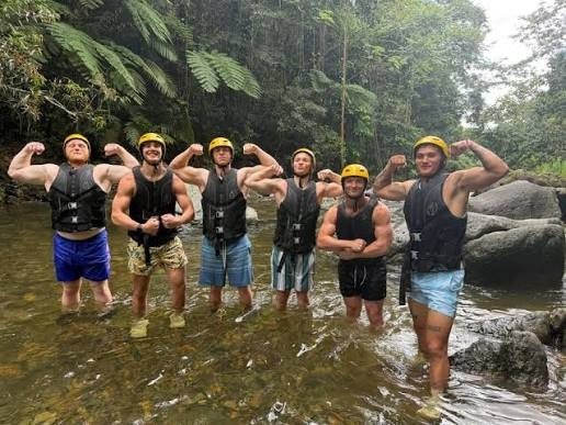 Grupo de amigos con casco y chaleco salvavidas posa dentro de un río poco profundo del bosque